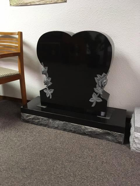 Jet black granite heart-shaped monument with carved rose and leaf relief on both sides, rough-cut base