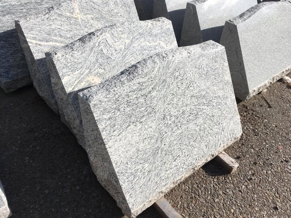 Close-up of raw gray granite slant blanks stacked on pallets showing natural swirling veining and texture of the stone before engraving
