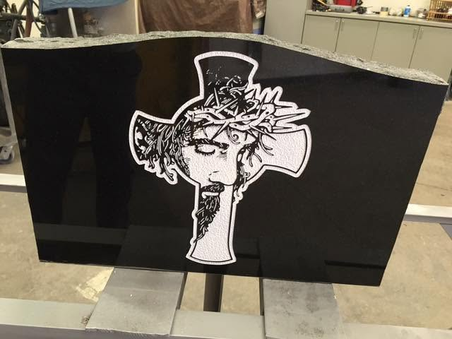Black granite slant with detailed engraving of Jesus Christ wearing crown of thorns on a cross, displayed in the workshop