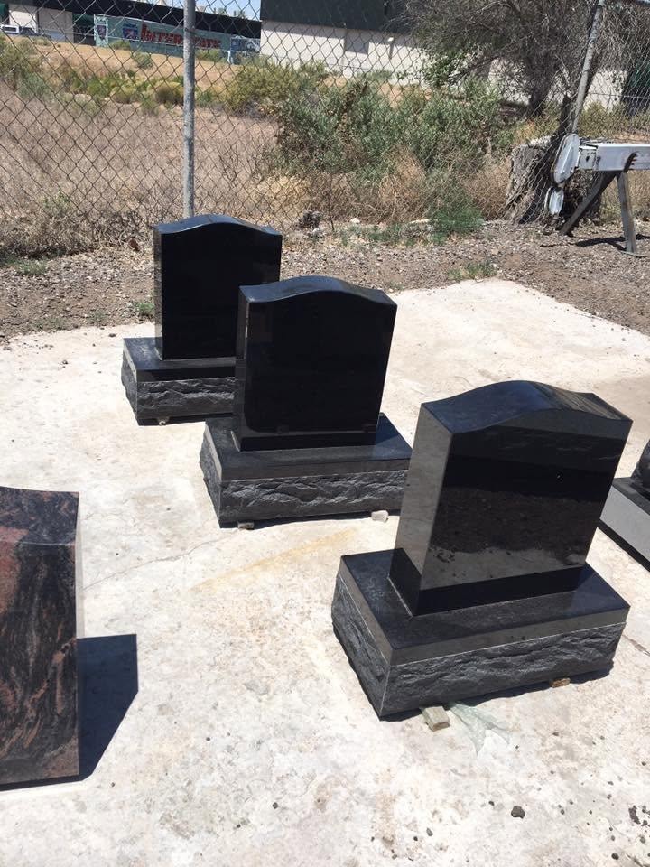 Three polished black granite upright monument blanks with rough-cut bases displayed outdoors in the Serenity Stone Co. yard, ready for custom engraving