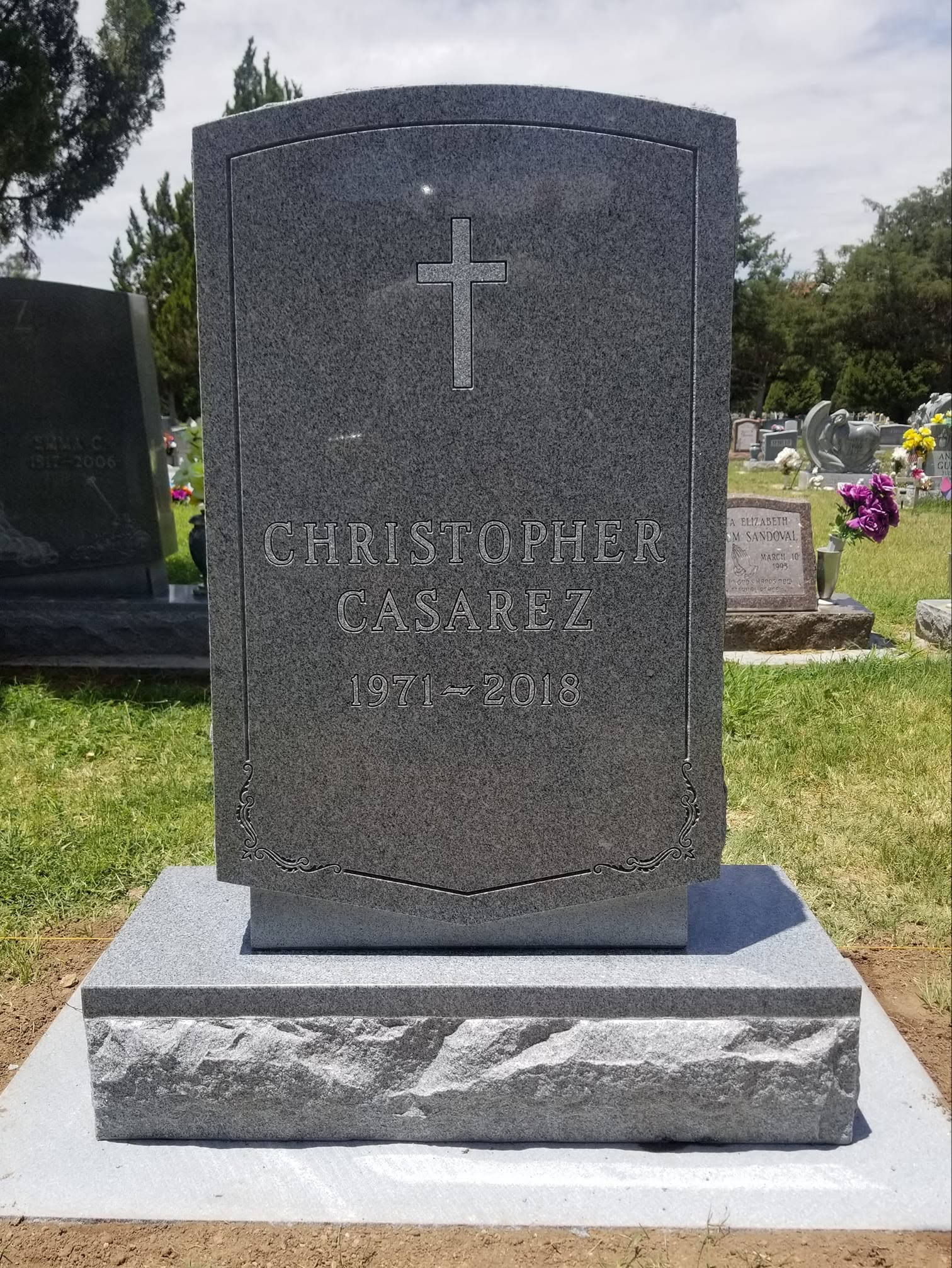 Christopher Casarez dark gray granite upright with engraved cross and decorative border on two-tier base