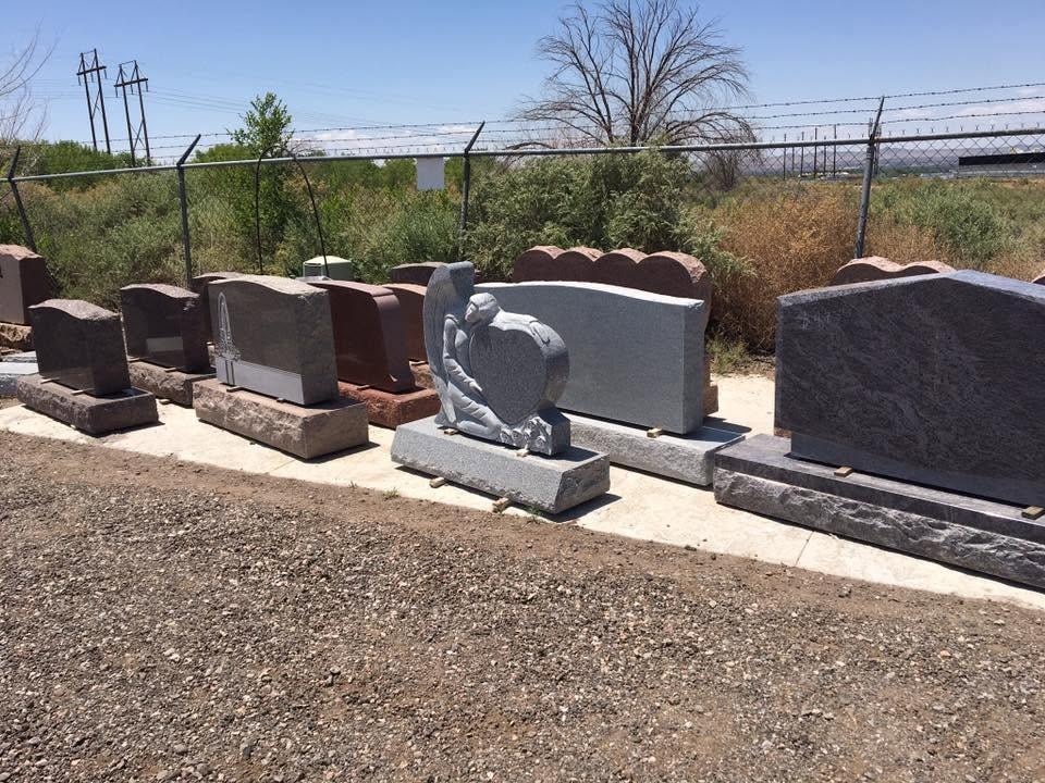 Serenity Stone Co. outdoor display yard showing a row of granite upright monuments in various colors including gray, red, and brown, with a gray angel holding a heart sculpture centerpiece