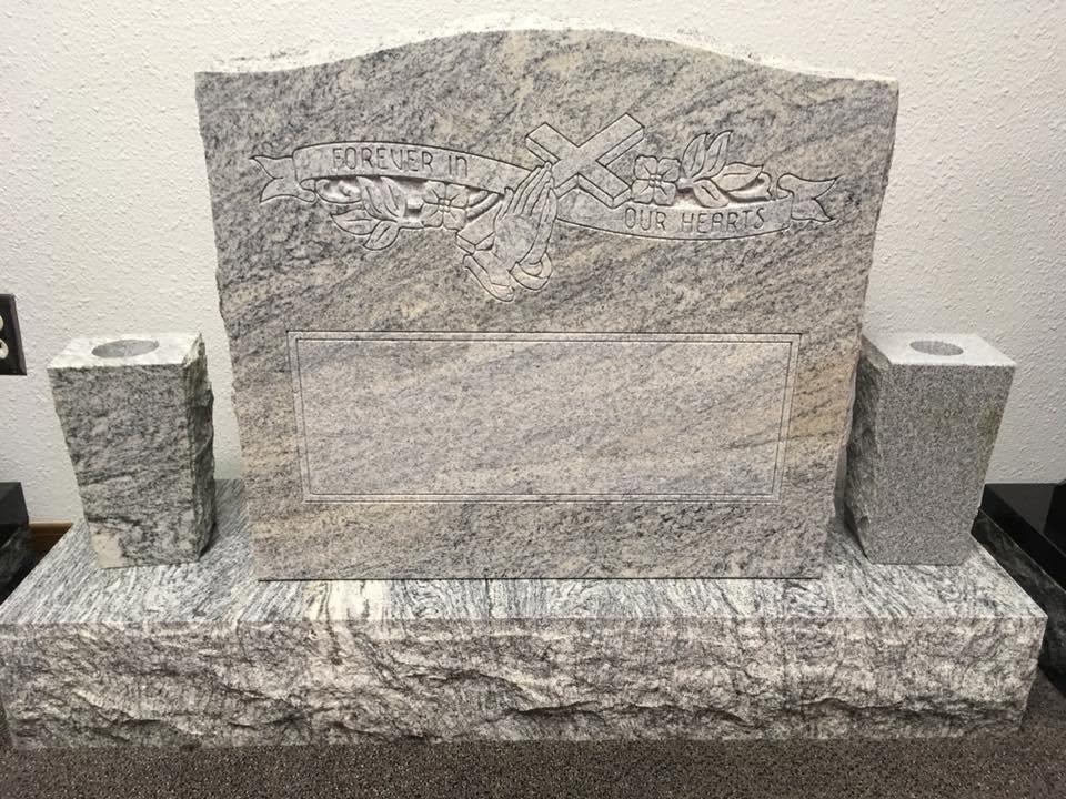Gray and white swirled granite bench-style upright monument with rough-cut natural edges, engraved praying hands, cross, and floral banner reading Forever In Our Hearts, blank name panel, and matching companion vase posts on each side