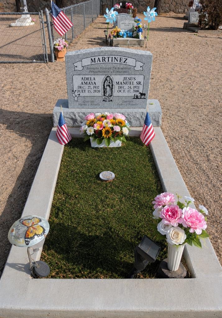 Martinez family gray granite double upright monument with Our Lady of Guadalupe engraving, American flags, and flower arrangements